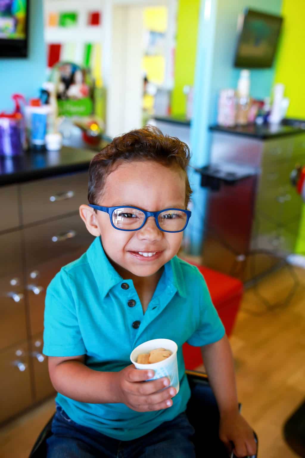 smiling boy wearing glasses sitting in pigtails & crewcuts franchise